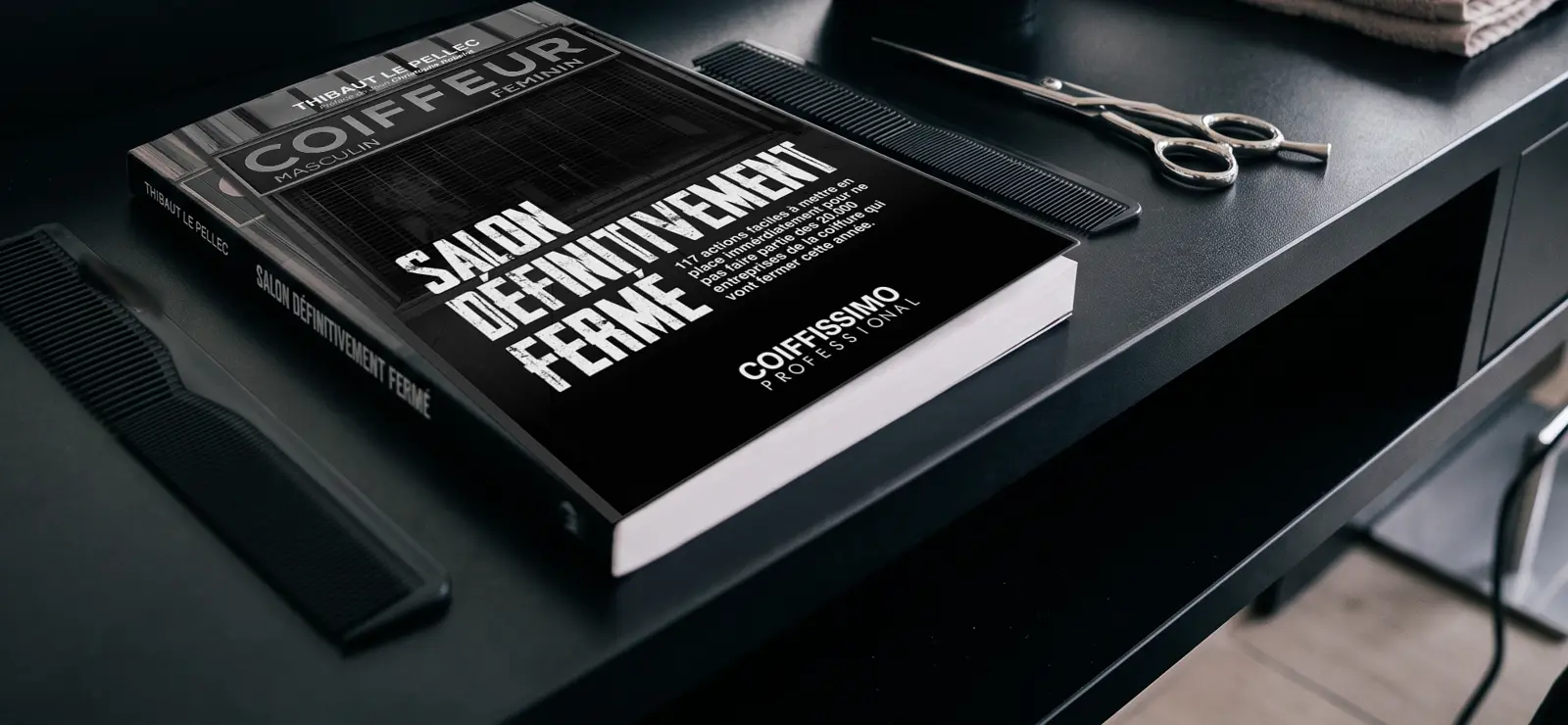 Le livre Salon définitivement fermé posé sur un poste de coiffure, à côté d'un peigne et d'une paire de ciseaux